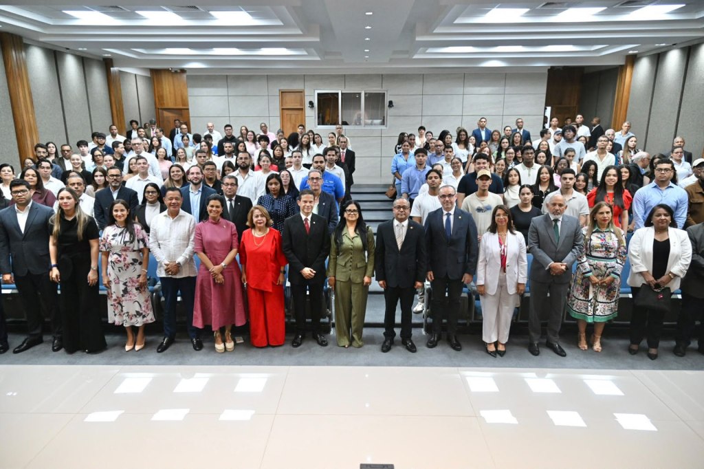 Grupo de personas posando en un auditorio, con un fondo de asientos y luces en el techo, todos mirando hacia la cámara.