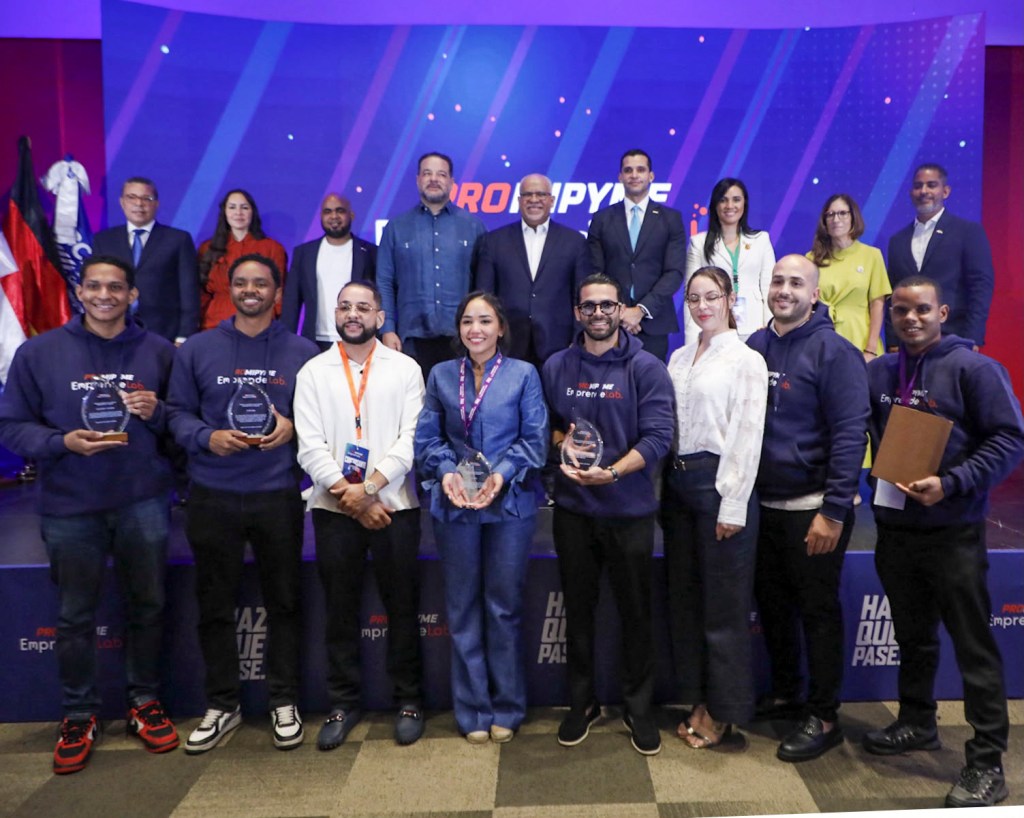 Un grupo de personas posando en un evento, sosteniendo trofeos, con un fondo de colores vivos y logotipos de la empresa, en un ambiente de celebración.