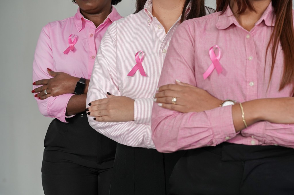 Tres mujeres con camisas rosas, cruzando los brazos, lucen cintas rosas en apoyo a la concienciación sobre el cáncer de mama.