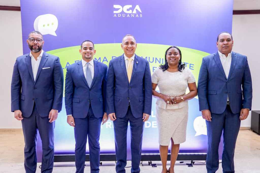 Grupo de cinco personas posando frente a un fondo que dice 'DGA ADUANAS'. Todos están vestidos con trajes formales.