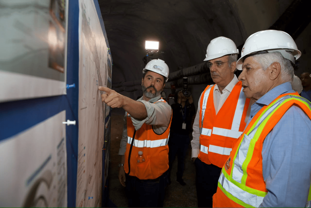 Tres hombres con cascos y chalecos de seguridad observan planos en un túnel.