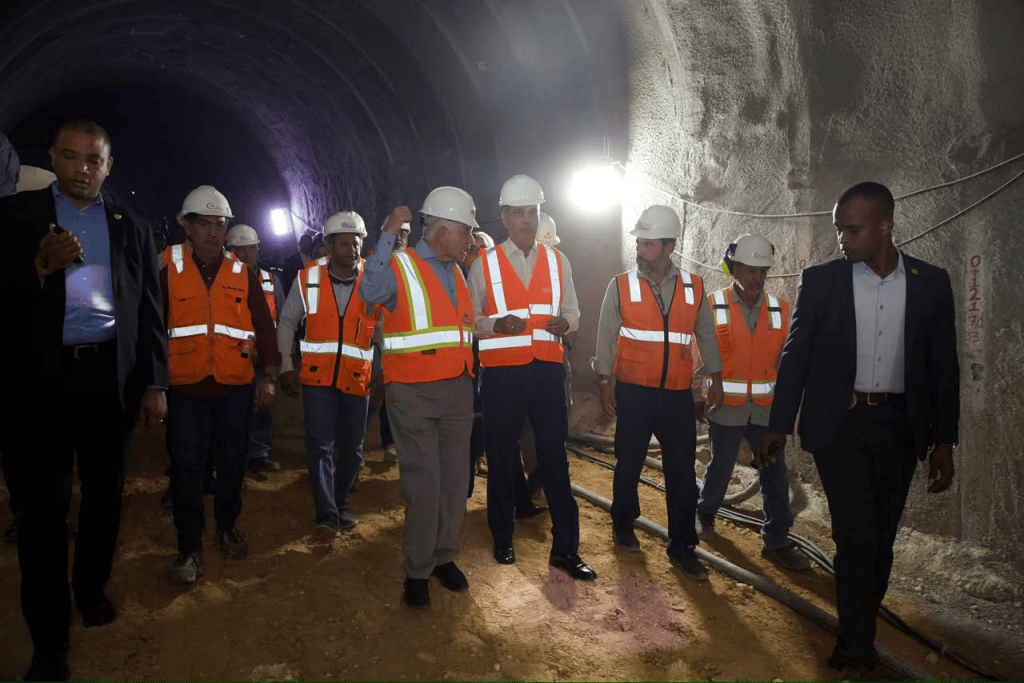 Grupo de trabajadores y funcionarios en un túnel, vistiendo cascos y chalecos de seguridad, durante una visita de inspección.