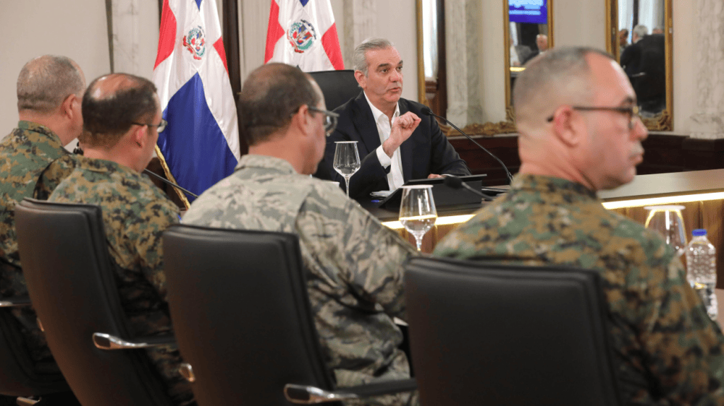 Reunión de líderes militares con un funcionario en un ambiente oficial, con banderas de la República Dominicana de fondo.
